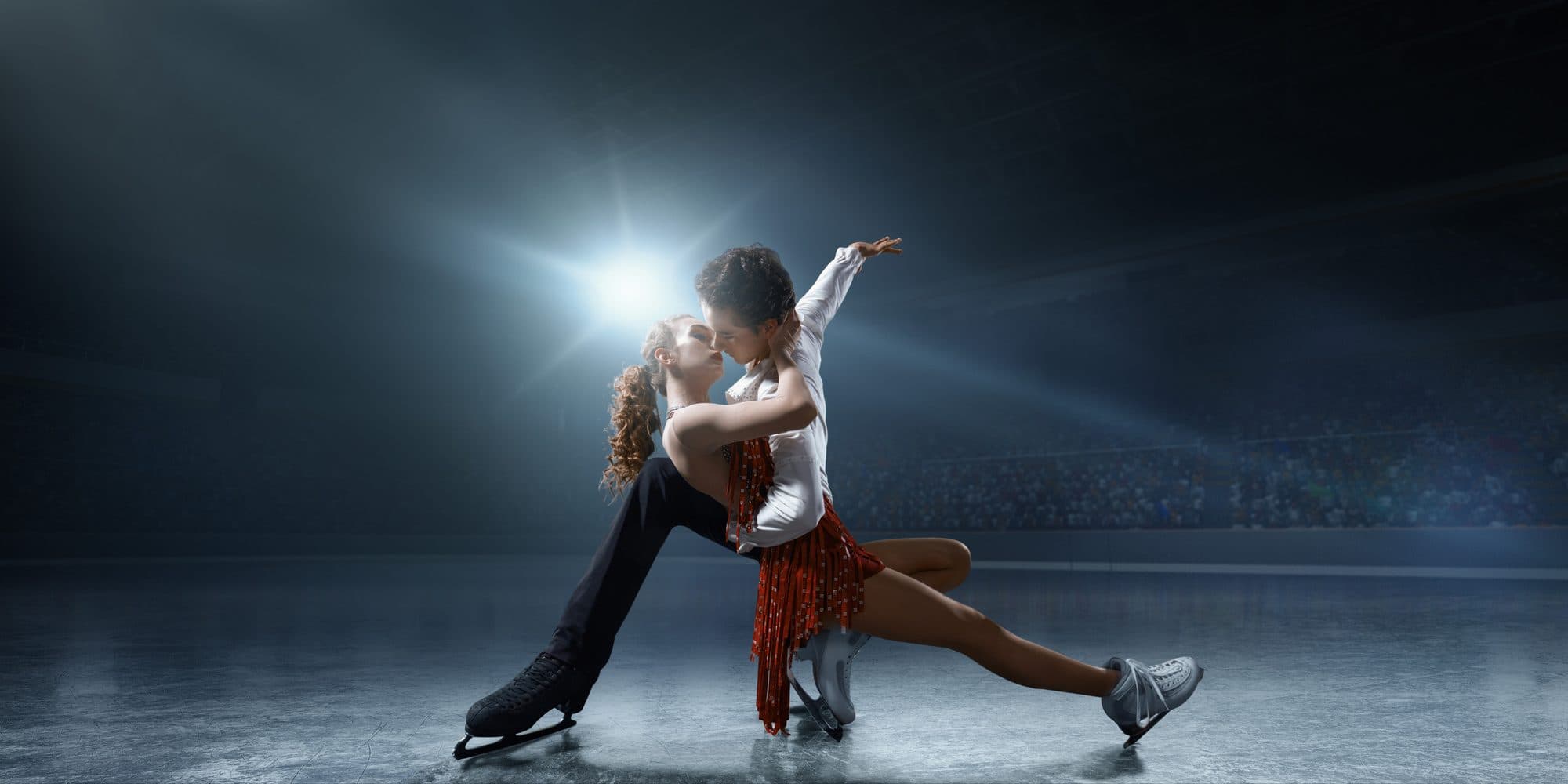 Two ice dancers in a dramatic lift under a spotlight
