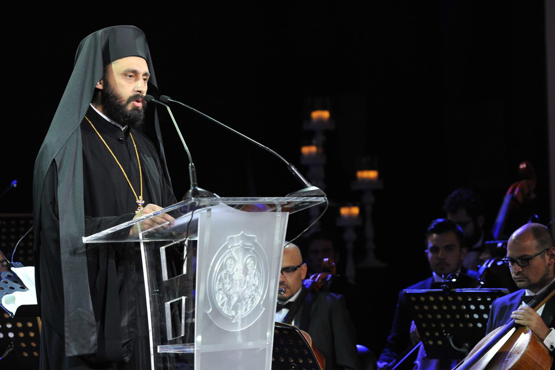 A bishop speaking at the podium in front of the orchestra