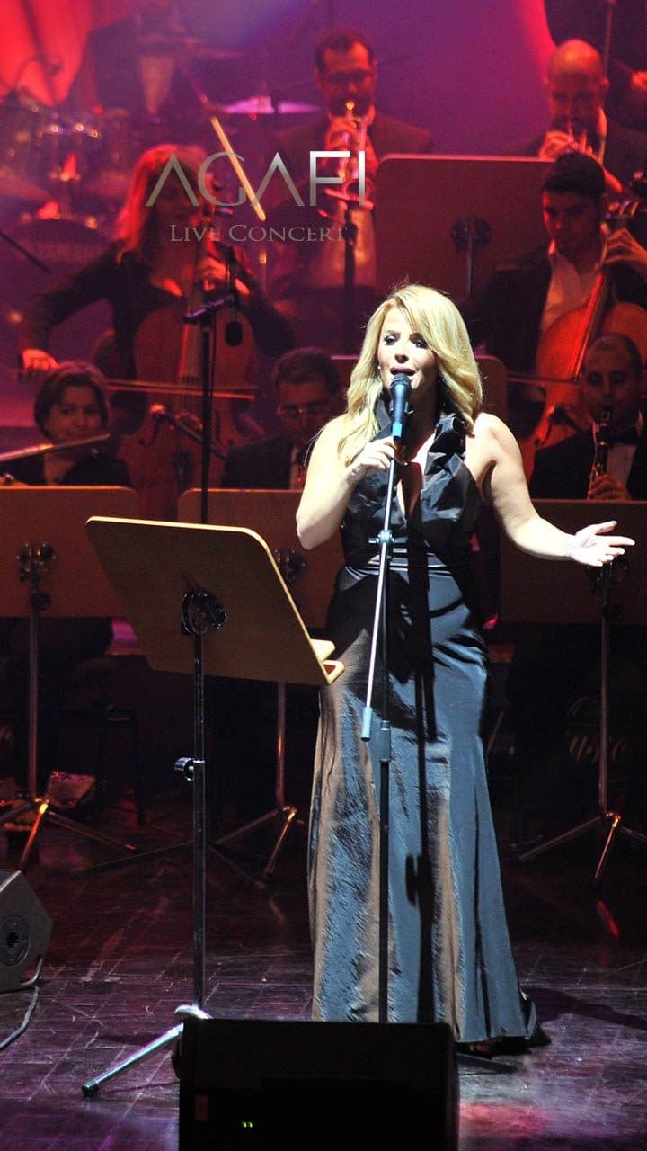 Singers and the orchestra on stage under orange and white light beams