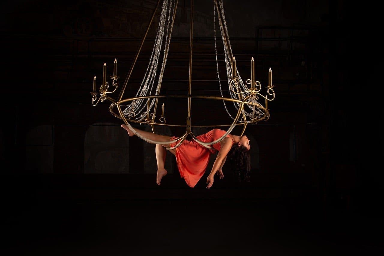 An aerialist in red lying in a suspended chandelier