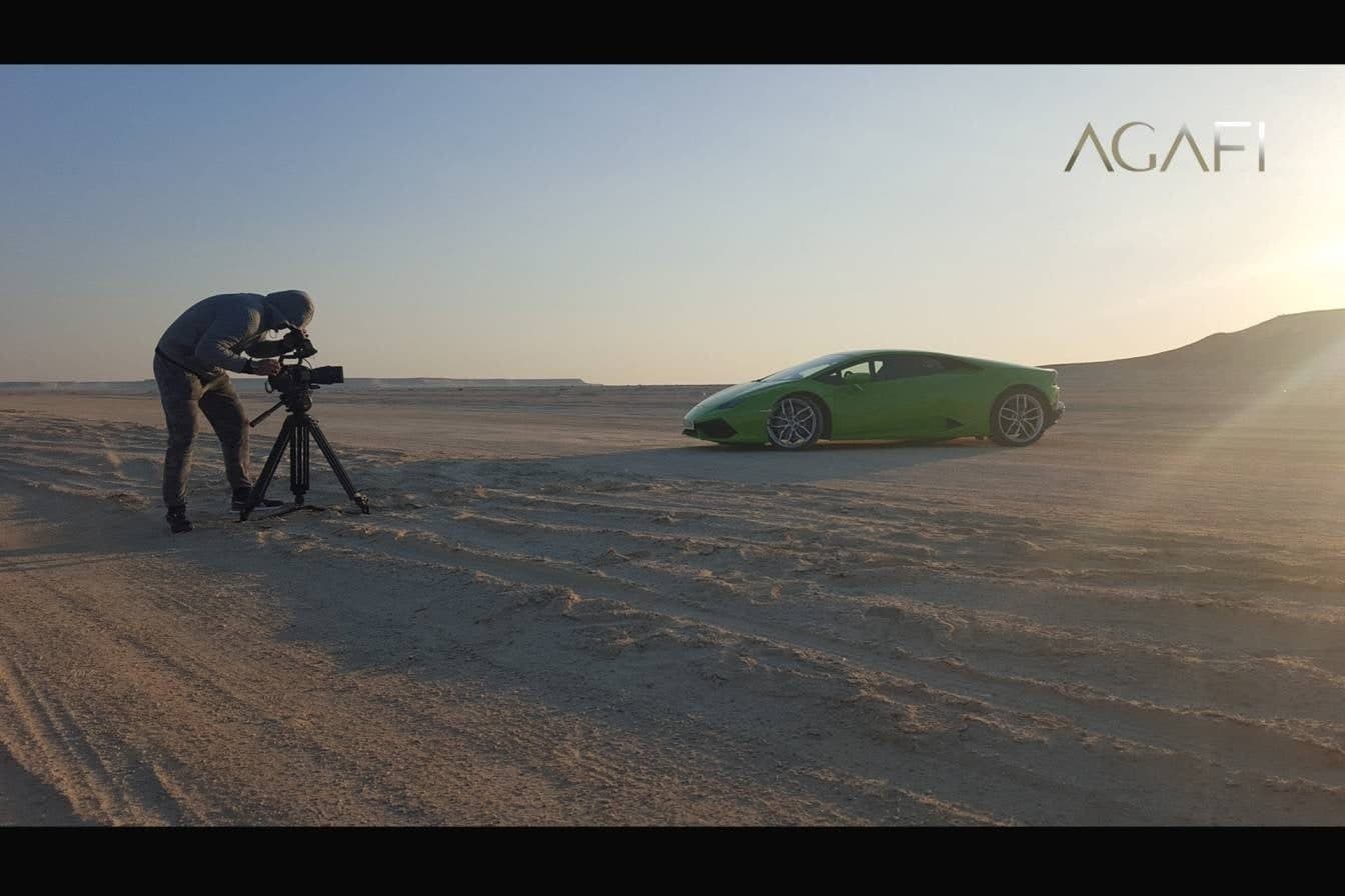 A camera operator filming a green Lamborghini on desert sand