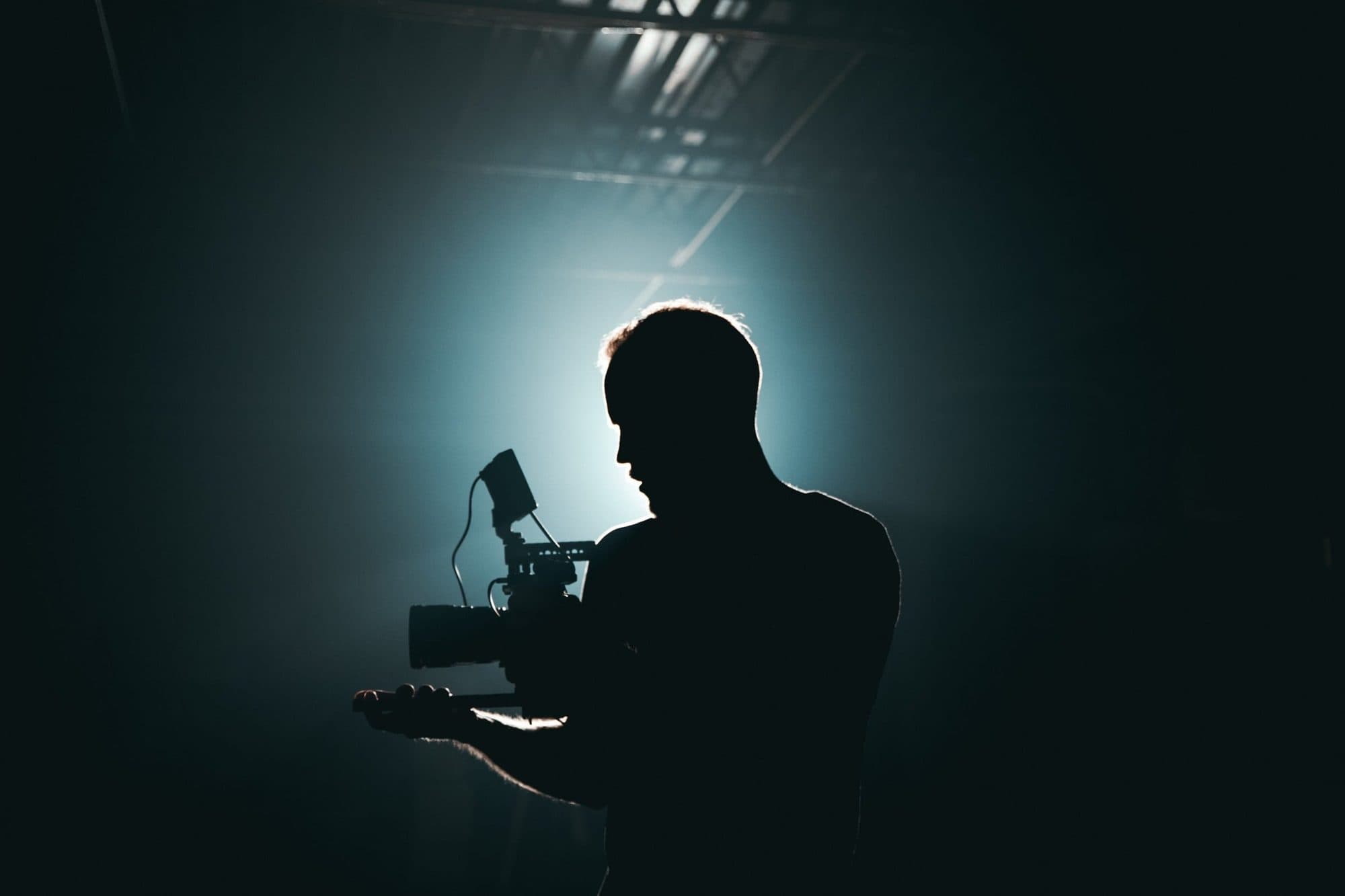 A camera operator in silhouette under a stage light