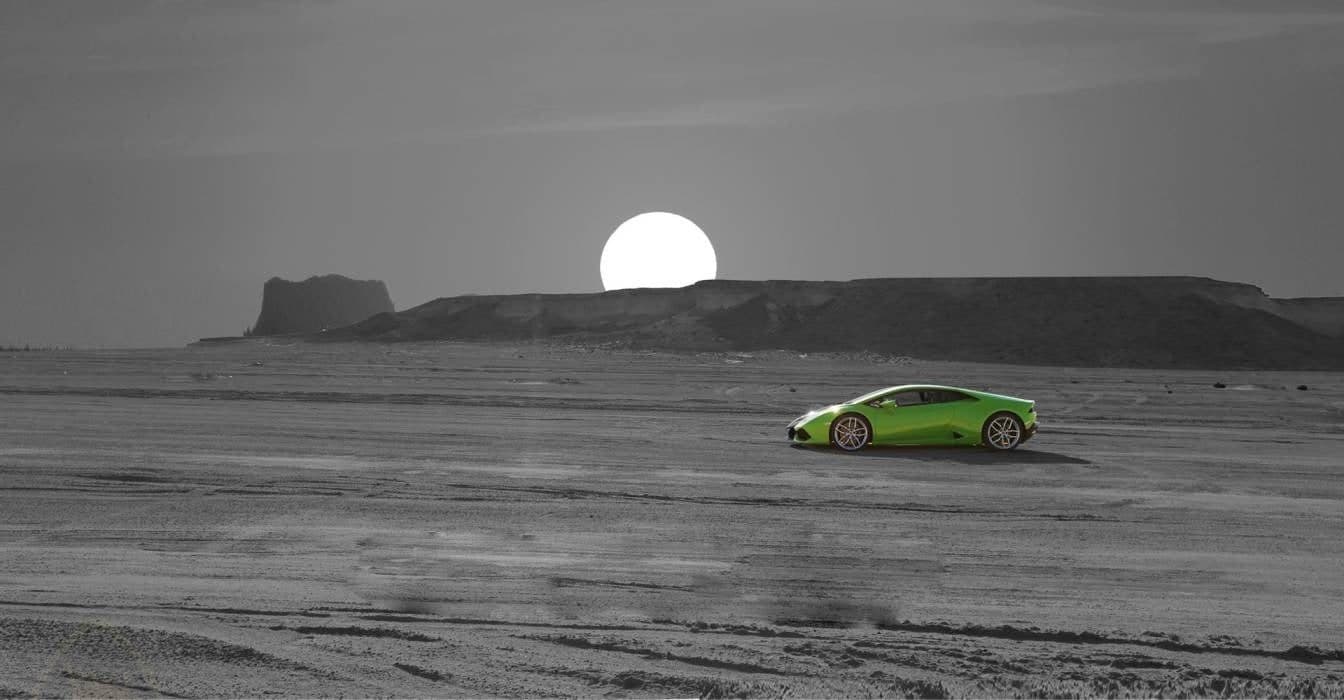 A green Lamborghini on a grey desert under a low sun